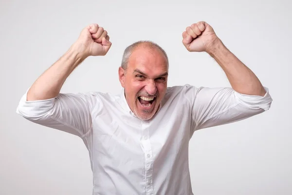 Homem hispânico maduro está feliz com sua vitória. Ele está segurando seus punhos e grito Wow . — Fotografia de Stock