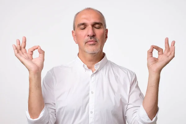 Konzentrierter reifer Mann im weißen Hemd versucht sich zu entspannen, träumt, hält die Finger zusammen. Meditation und Entspannungskonzept. — Stockfoto