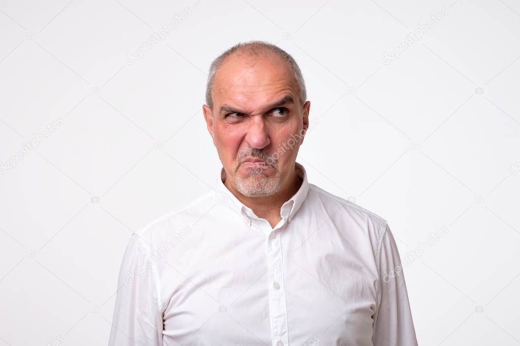 worried suspicious mature hispanic man isolated against white studio background. His face is in disgust grimace.
