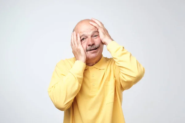 Старший латиноамериканец в жёлтой футболке натягивает кожу на лицо руками. Он боится или устал от стресса. . — стоковое фото