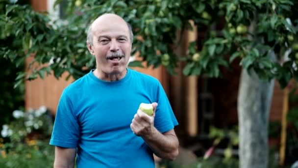 Καυκάσιος ανώτερος άνθρωπος σε μπλε tshirt τρώει φρέσκο μήλο εξωτερική — Αρχείο Βίντεο