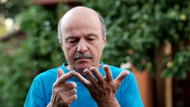 Kaukasischer Senior, der an den Fingern zählt, bis fünf vor dem Hintergrund eines grünen Gartens steht — Stockvideo