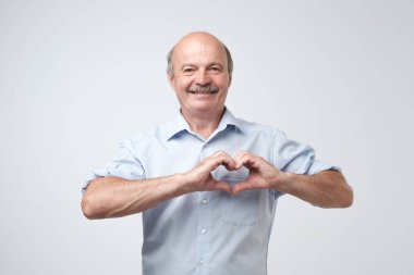 ellerini kalbinde öpüşürken mavi gömlekli yaşlı beyaz adam. Bağış işinde çalışmak, sağlık veya aşık olmak