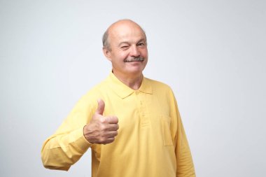 Sarı tshirt beyaz arka plan üzerinde göz kırpıyor iyimserlik işareti onun başparmak ile yakışıklı, kel adam
