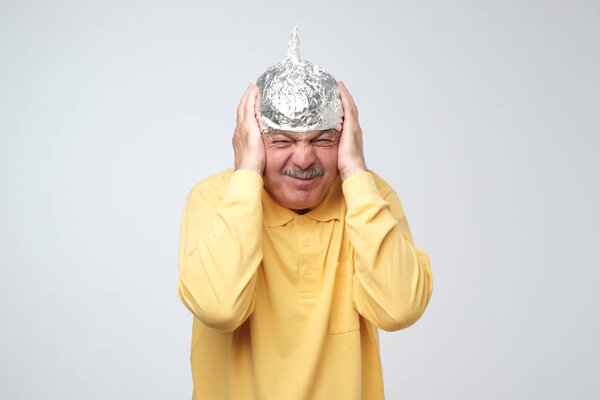 Caucasian mature man in a tin foil hat displeased hiding from outdoor life. Afraid of radiation, loud sounds or aliens
