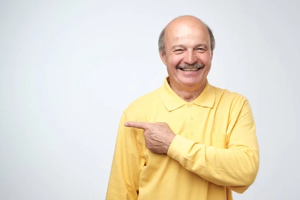 Happy Senior Man Yellow Tshirt Looking Camera Smiling Pointing Aside — Stock Photo, Image