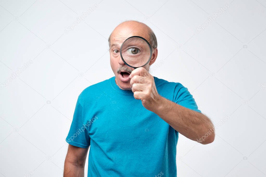 Elderly man in blue t-shirt looking through a magnifying glass. Concept of quality control checking. Let me see all the benefits