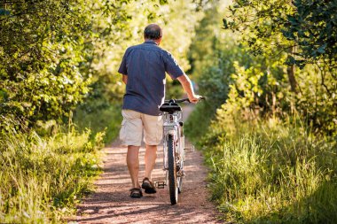 Olgun adam kadar sonuna kadar bisiklet ile orman yolundaki yürüyor