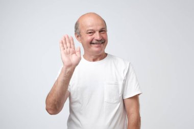 Beyaz tişört içinde çekici Avrupa emekli dostu arıyorum Merhaba jest elinde neşeyle gülümseyen süre ihlalinden. Dedesi torununu karşılama. Seni gördüğüme çok sevindim.