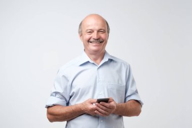 Metin mesajı yazmaya. Gülümseyen kıdemli adam beyaz izole arka plan üzerinde duran ve cep telefonu tutan bıyıklı.