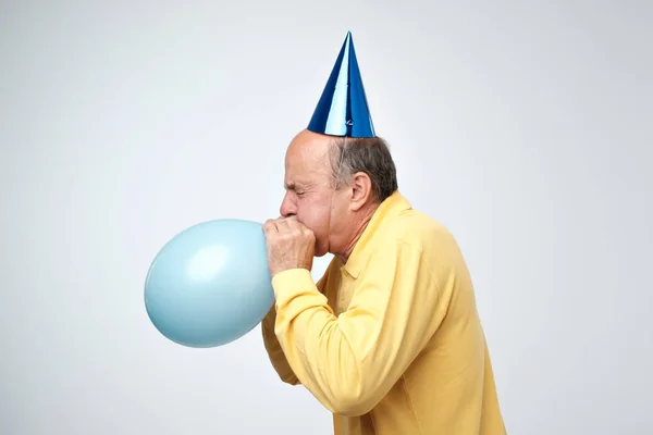 Portrait Mature Man Yellow Tshirt Funny Cap Blowing Blue Balloon — Stock Photo, Image