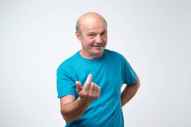 Mavi oynak kıdemli yetişkin kapalı portresi gösterilen t-shirt burada işaret parmağı ve gri arka plan üzerinde gülümseyen jest gel. Korkuyor gibi değil, ben değil lokma