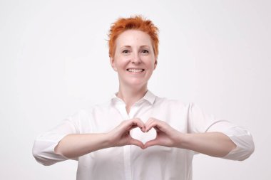 Bir kalp yapma romantik Olgun Kızıl saçlı kadın onun aşk ve sevgi mutlu bir ihale gülümseme ile gösterilen göğsünün önünde parmaklarını jestle. Sağlık kavramı