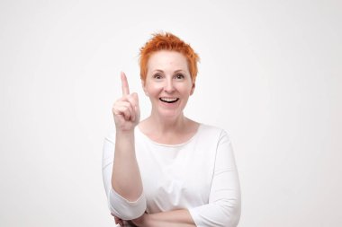 Onun parmak eureka işareti, anlayış veya çözüm gösteren beyaz arka plan üzerinde izole beyaz t-shirt giyen kızıl saçlı enerjik gülümseyen güzel fotoğraf. O yenilikçi fikri vardır