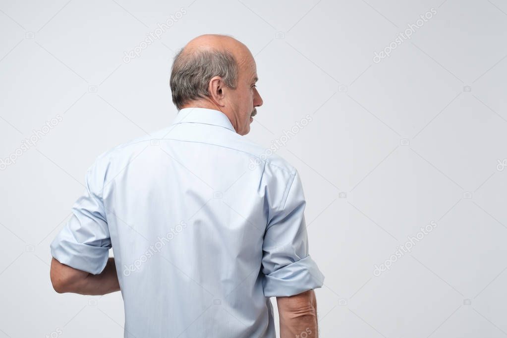 Back view of senior bald caucasiant man in casual shirt on gray background