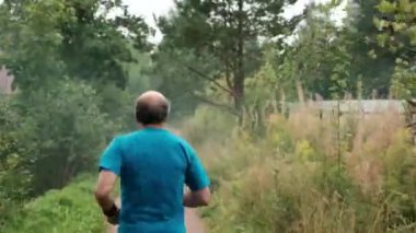 Ağaçlar yolda koşan olgun adam. Arkadan görünüm.