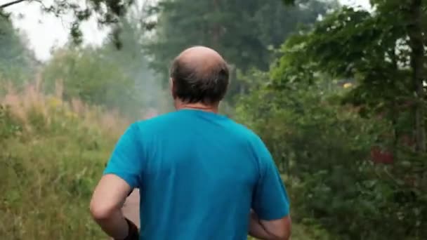 Homme mûr courant sur la route à travers les arbres. Vue arrière . — Video