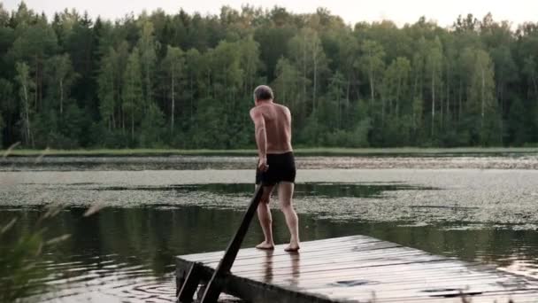 Caucasien mature homme sautant de jetée en bois dans le lac . — Video