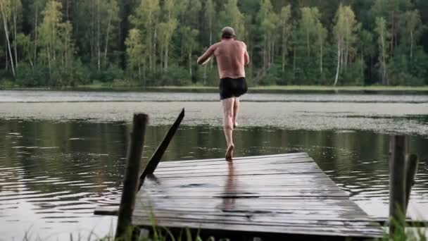Взрослый кавказский мужчина прыгает с деревянного пирса в озеро . — стоковое видео
