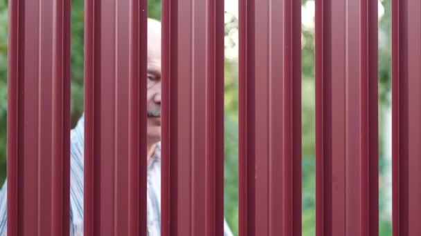 Senior man die door zijn buurman bespioneren hek — Stockvideo