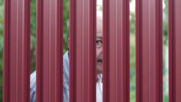 Hombre mayor mirando a través de la cerca espiando a su vecino — Vídeos de Stock