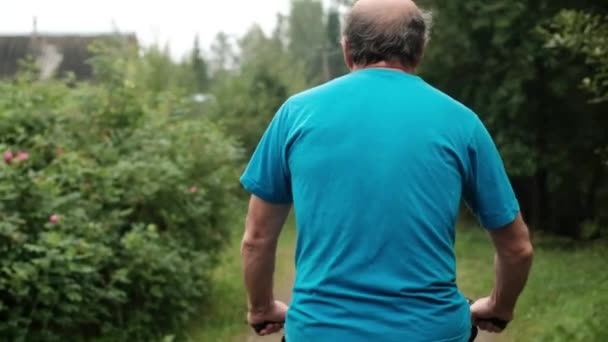 Senior caucasian male in blue t-shirt enjoying his summer vacation riding a bicycle outdoor between trees. — Stock Video