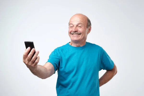 Sorrindo feliz homem sênior com bigode tirar uma selfie com seu telefone e enviá-lo para sua família . — Fotografia de Stock