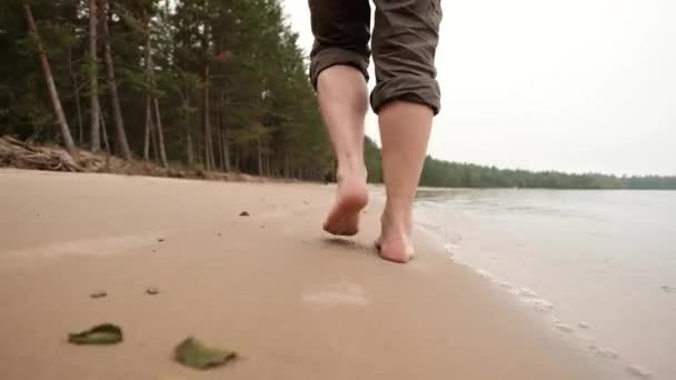 Die Beine eines kaukasischen Mannes, der auf Sand in Wassernähe geht — Stockvideo