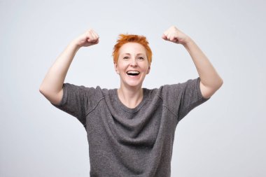 Onun gücü ve olumlu ruh hali gösteren yükseltilmiş yumrukları ile gülümseyen neşeli olgun kadın.