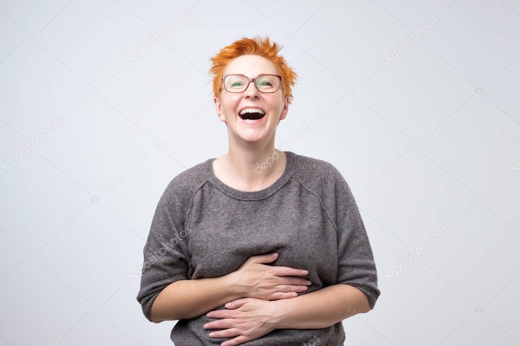 Close up portrait of a beautiful mid adult woman with red hair laughing standing on gray background.