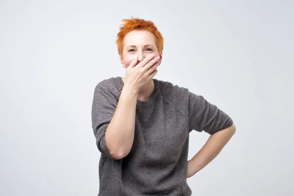 Divertente donna matura con i capelli rossi corti chiudendo la bocca con il palmo dell'udito divertente scherzo . — Foto Stock