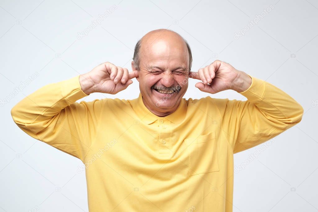 Using natural earplugs not to hear spoilers. Good-looking happy mature european man smiling with closed eyes