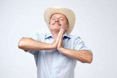 Memnun umutlu olgun adam gözlerini kapatır, avuç içi birlikte, iyi şanslar, için dua ediyor tutar gri arka plan üzerinde izole dreamful görünüme sahip. Eski kovboy isteyen Tanrı'nın faydaları