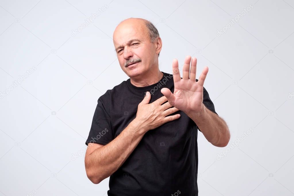 Displeased mature man refusing, stretching hands to camera over grey background. I do not want to have deal with you concept