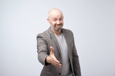 Gülümseyen izole neşeyle gri arka plan üzerinde iken Merhaba hareketle bir el veren dostu görünümlü çekici Avrupa bir adam. Birlikte komutta çalışalım