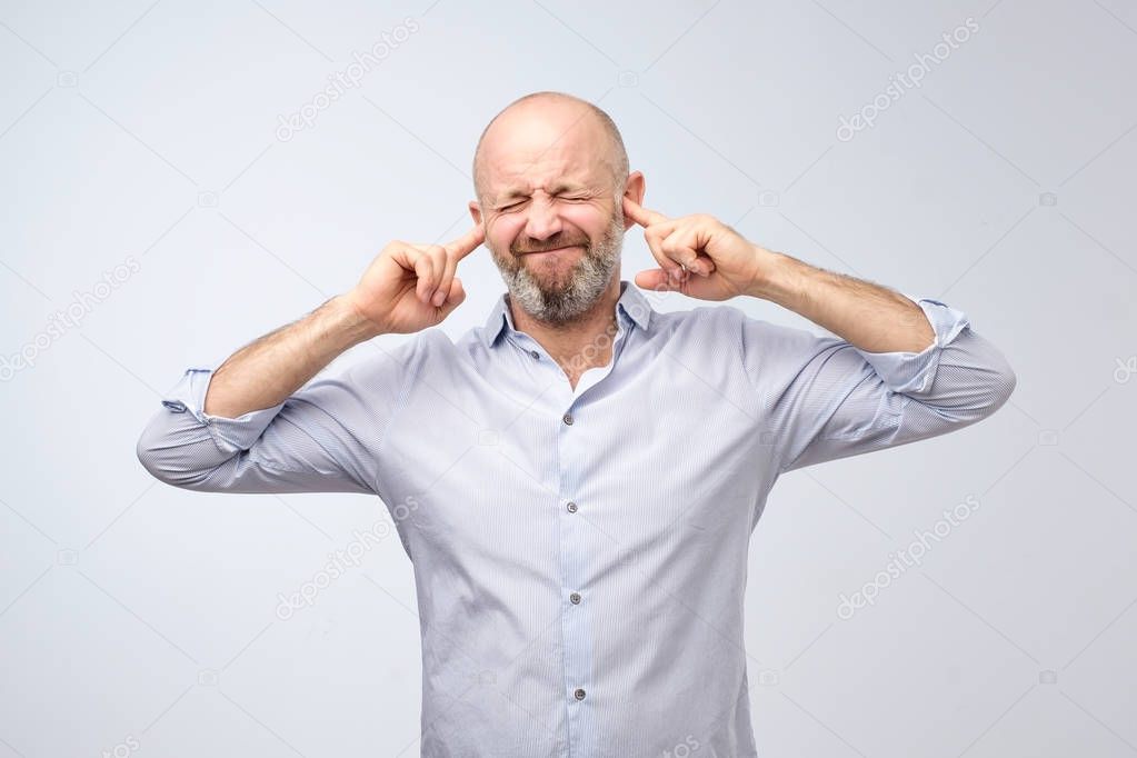 Annoyed mature man plugging ears with fingers. I do not want to hear these gossips
