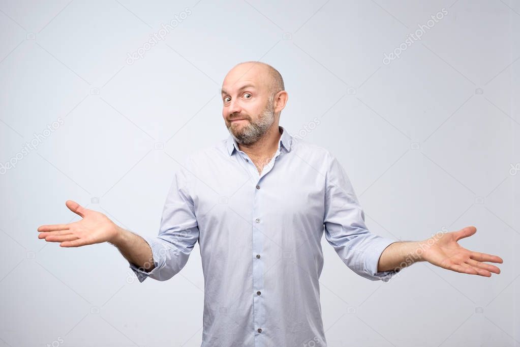 Confused mature bearded man standing and shrugging shoulders isolated over white background. I do not know the solution of this problem concept