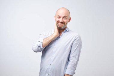 Sakallı hoş sevimli Avrupa erkek getirmek el towardfacewith çok güzel ifade alma sanki iltifat veya gri arka plan üzerinde duran kendini öven.