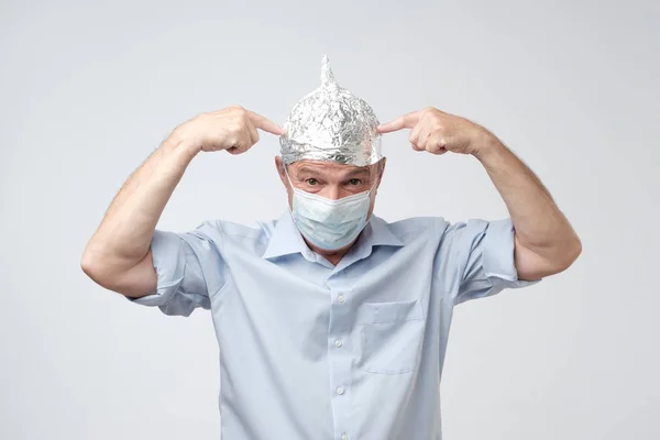 Caucasian mature man in a tin foil hat and medical hat displeased hiding from outdoor life.