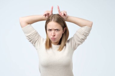 İnatçı olduğumu. Gri arka plan üzerinde çatık şirin duygusal kadın sanki gibi onun'boynuzları, başının arkasında işaret parmakları ile işaret eden oktan yukarı çiller ile.