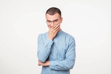 Gülüyor ve beyaz arka plan üzerinde el ile ağzını kapsayan genç adam portresi. Bazı kişi rahatsız değil bir kahkaha tutmaya çalışıyorum. O sadece komik bir fıkra duydum