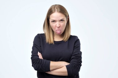 Dissatisfied woman frowns face, has disgusting expression, shows tongue, expresses disgust, irritated with somebody clipart