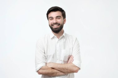 Çapraz kolları üzerinde gri arka plan izole olan ayakta beyaz tişörtlü yakışıklı İspanyol adam gülümseyen portresi