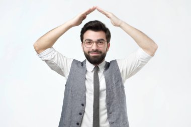 Holding ile neşeli adam bitti kafası gri arka plan üzerinde bir çatı ev gibi eller. Bir yeni daire veya ev satın almak.