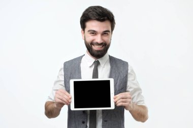 Neşeli genç hsipanic adam holding tablet ile gri arka plan üzerinde boş perde