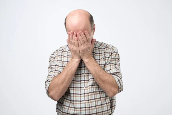 Älterer Mann leidet unter schmerzhaften Gefühlen, wenn er den Kopf nach unten beugt und das Gesicht mit Handflächen bedeckt — Stockfoto