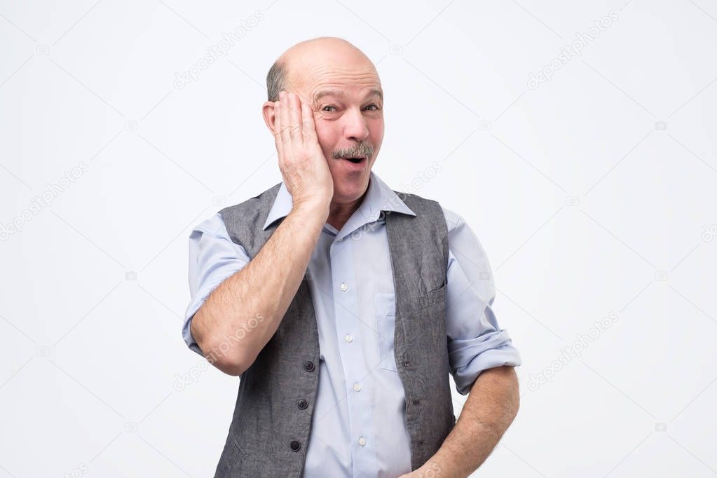 Joyful over-emotive senior man, yelling from pleasure and surprise, holding palm on cheeks