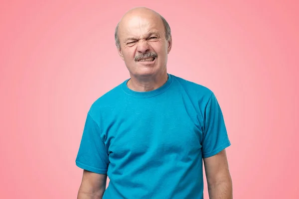 Mogen vuxen i blå t-shirt med tvekan med avsmak på ansikte står på rosa bakgrund. — Stockfoto