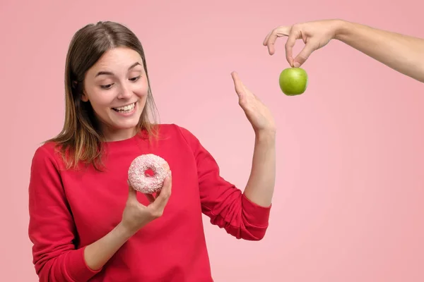 果物とお菓子との間を選択する赤い服の美しい若い女性 — ストック写真