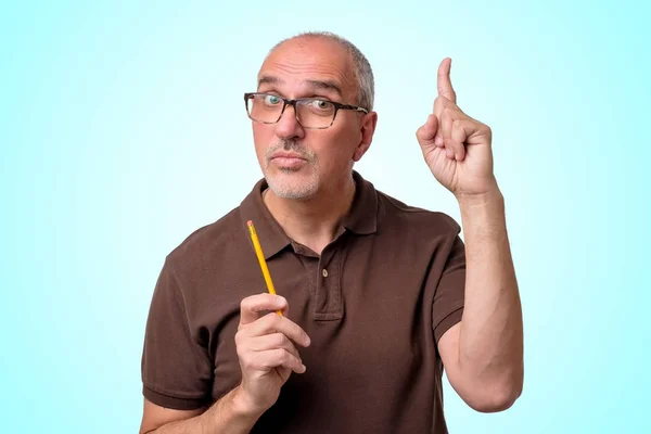 Volwassen Spaanse man heeft een goed idee staan op blauwe achtergrond. Leraar houdt potlood. — Stockfoto